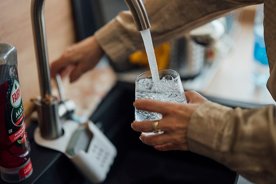 Person filling a glass of water at a kitchen sink